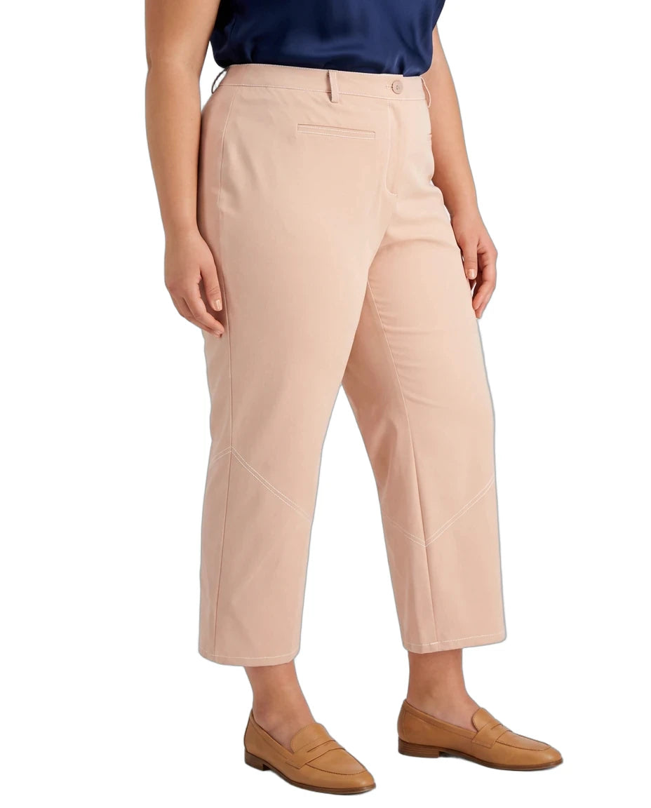 A model wearing a pair of cropped, straight-leg trousers in a light peach-beige color, styled with a navy blue top and tan loafers against a plain white background.
