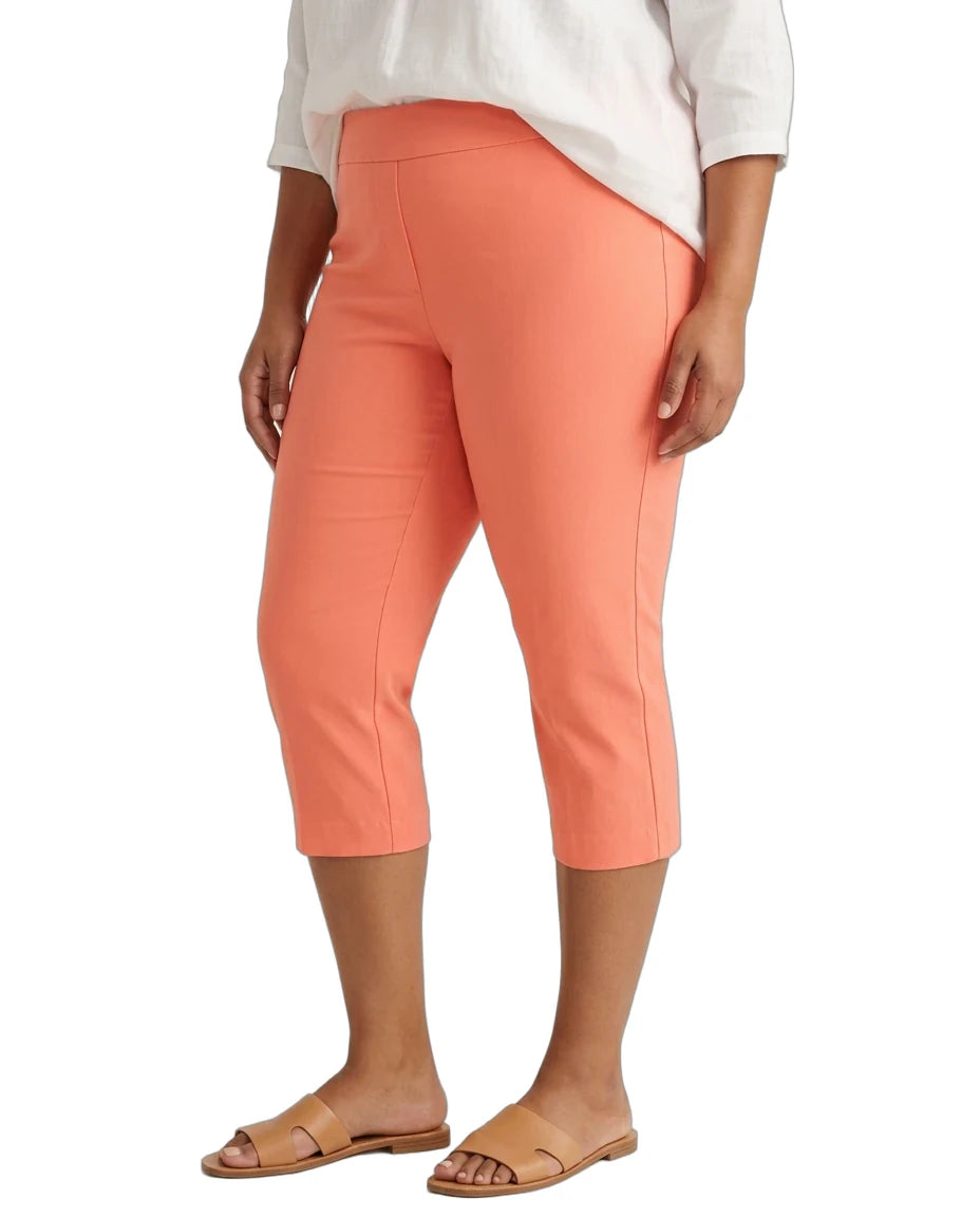 A model wearing coral orange capri pants, a white top, and tan slide sandals, shown from the waist down against a plain white background.