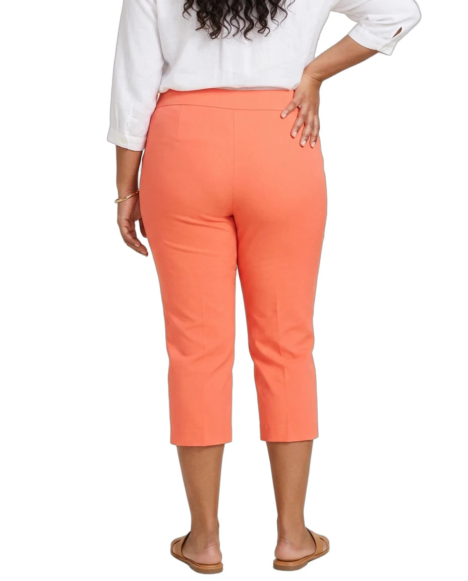A woman shown from the back wearing bright coral-orange cropped capri pants, a white blouse, and tan flat sandals against a plain white studio background.