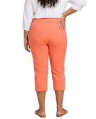 A woman shown from the back wearing bright coral-orange cropped capri pants, a white blouse, and tan flat sandals against a plain white studio background.