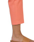 A close-up of a person's lower leg and foot wearing cropped peach-pink trousers and tan slide sandals against a plain white background.