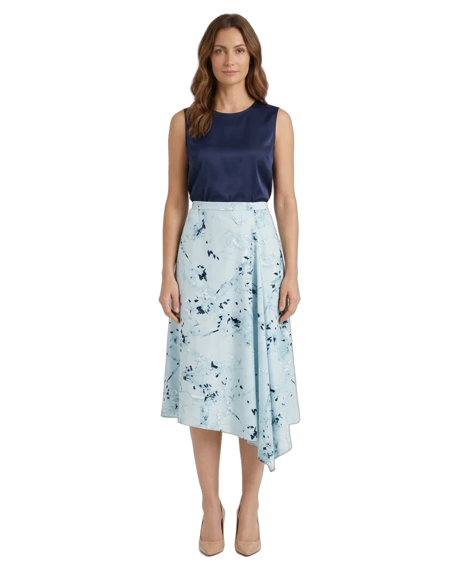 A woman modeling a sleeveless midi dress with a dark navy blue satin bodice and a light blue wrap-style skirt featuring a dark blue abstract floral print, set against a plain white background.