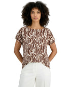 Woman wearing a brown and white patterned top with white pants on a white background