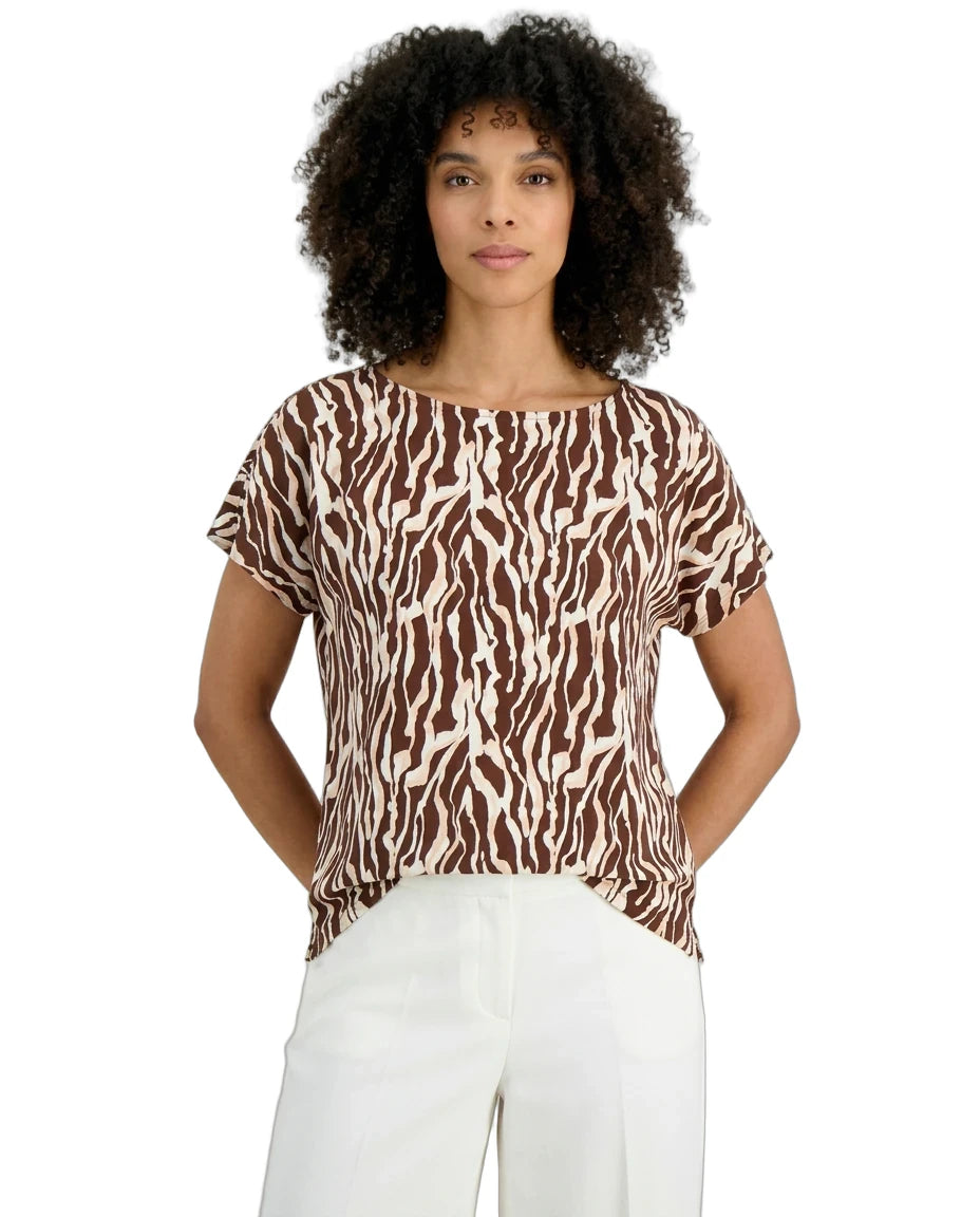 Woman wearing a brown and white patterned top with white pants on a white background