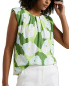 Woman wearing a green floral sleeveless top with white pants on a plain background