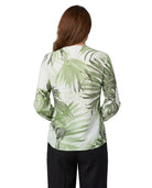 A woman viewed from the back wearing a long-sleeve blouse with a green palm leaf pattern on a white background, paired with black pants, against a plain white studio background.