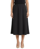 A woman modeling a black midi skirt with a gathered waistband, paired with beige heels, shown against a plain white background.
