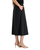 A model wearing a black midi skirt with side pockets, paired with beige slingback heels, shown from the waist down against a plain white background.