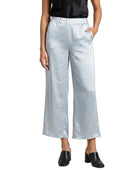 A model wearing light silver wide-leg cropped pants with an elastic waistband, styled with a black satin top and black leather mule shoes against a plain white background.