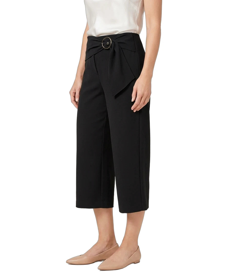 A model wearing black cropped wide-leg pants with a matching fabric tie belt and round metal buckle, styled with a white top and beige flats against a white background.