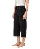 A model wearing black cropped wide-leg pants with a matching fabric tie belt and round metal buckle, styled with a white top and beige flats against a white background.