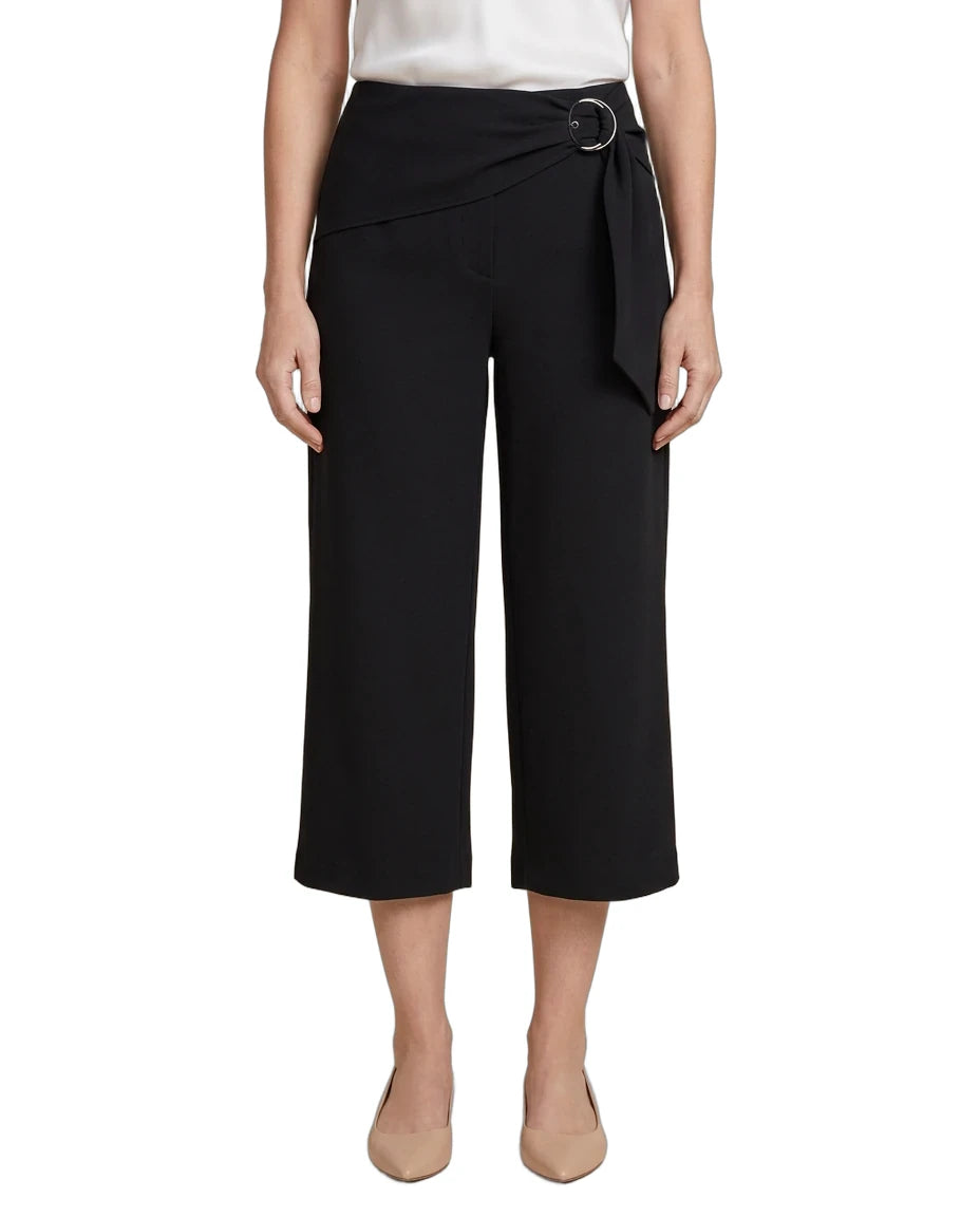 A model wearing black cropped wide-leg pants with a wrap-style waist and a silver-tone circular belt buckle, paired with a white top and beige heels against a plain white background.