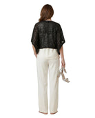 Woman wearing a black sequin top and white pants on a white background
