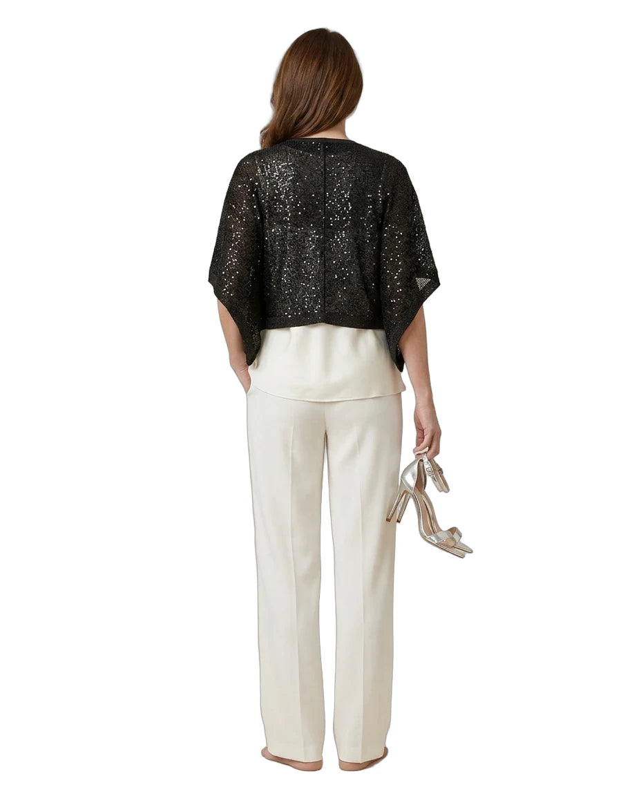 Woman wearing a black sequin top and white pants on a white background