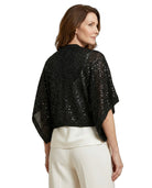Woman wearing a black sequin top and white pants on a white background