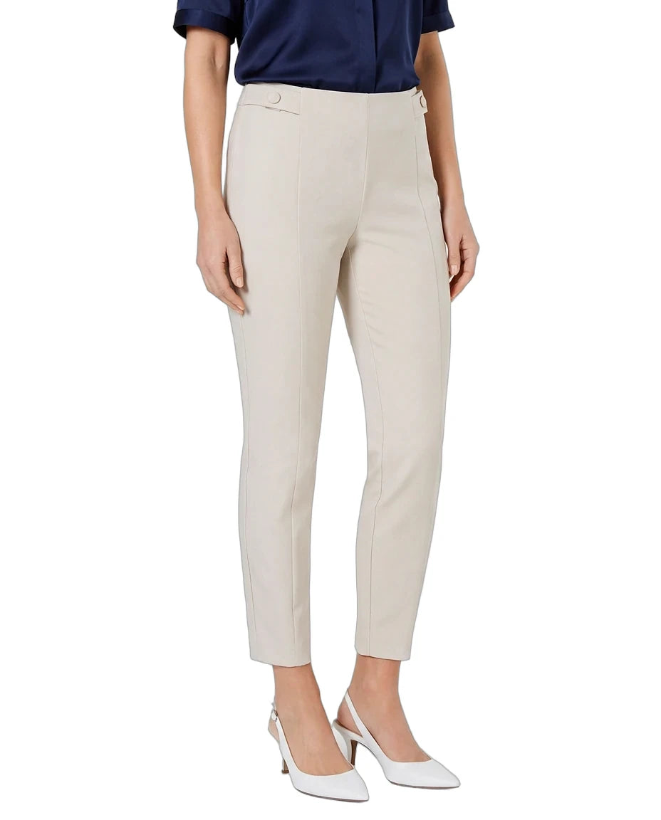 A model wearing a pair of slim-fit, ankle-length cropped trousers in a light beige color, styled with a navy blue top and white pointed-toe heels against a plain white background.
