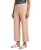 A model wearing light peach-pink cropped trousers with diagonal seam details on the lower legs, styled with a dark gray top and white slide sandals against a plain white background.