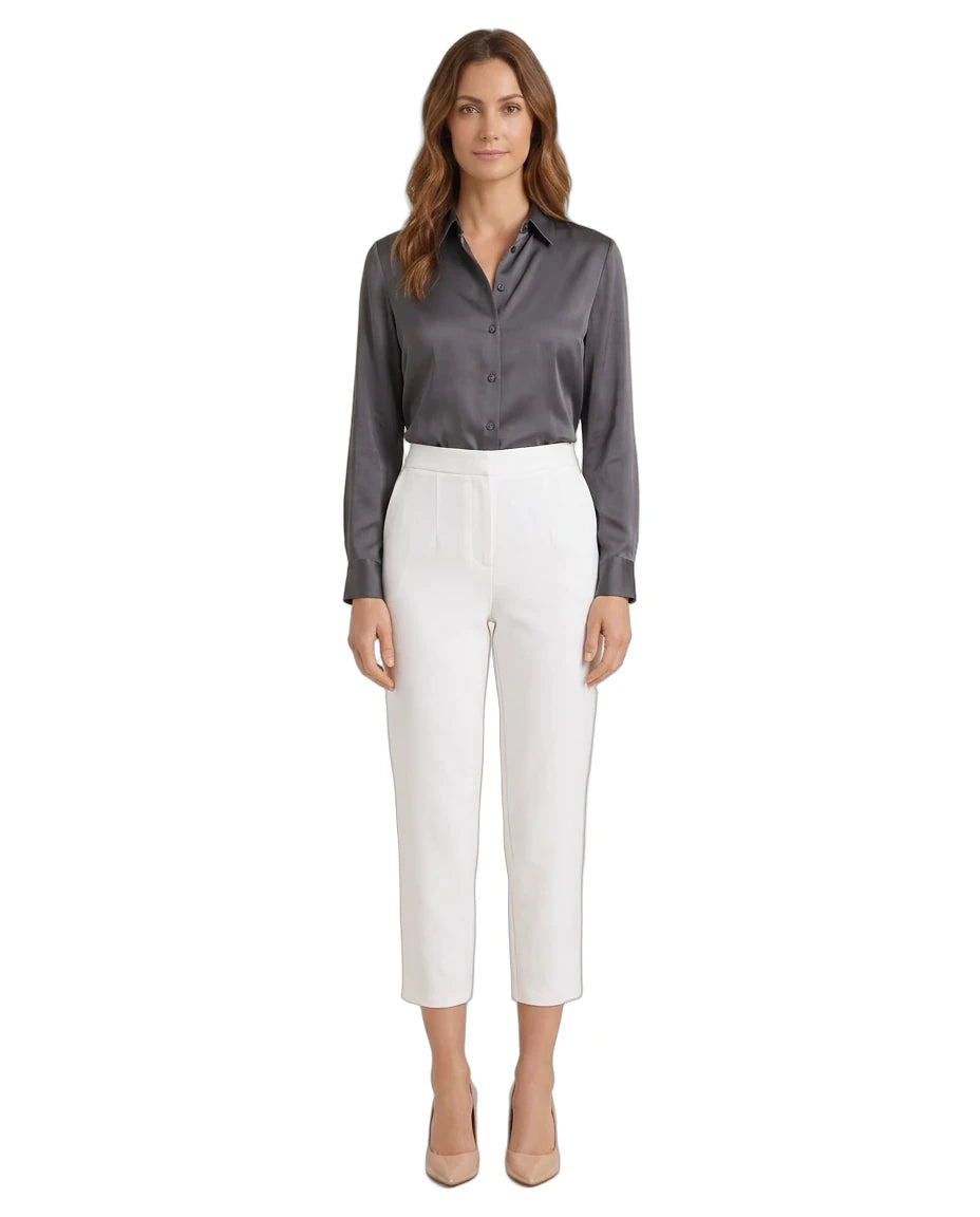 A woman modeling a dark gray satin button-down shirt and white cropped trousers, standing against a plain white background.