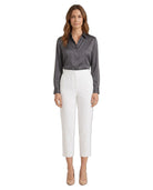 A woman modeling a dark gray satin button-down shirt and white cropped trousers, standing against a plain white background.