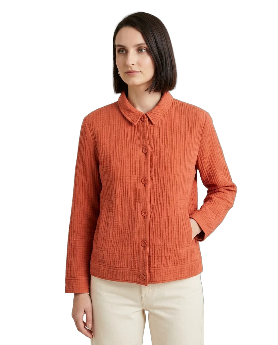 A woman wearing a textured, ribbed orange cardigan with a button-down front and collar, paired with cream pants, against a plain white background.