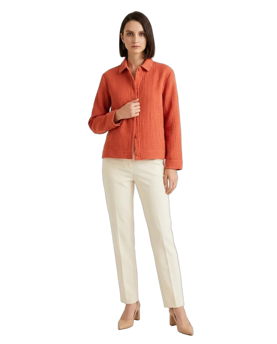 A woman modeling a textured orange button-up shirt paired with off-white trousers and beige heels, set against a plain white background.