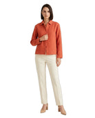A woman modeling a textured orange button-up shirt paired with off-white trousers and beige heels, set against a plain white background.