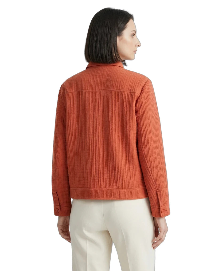 A woman shown from the back wearing a textured rust-orange quilted jacket and cream-colored trousers, photographed against a solid white background.