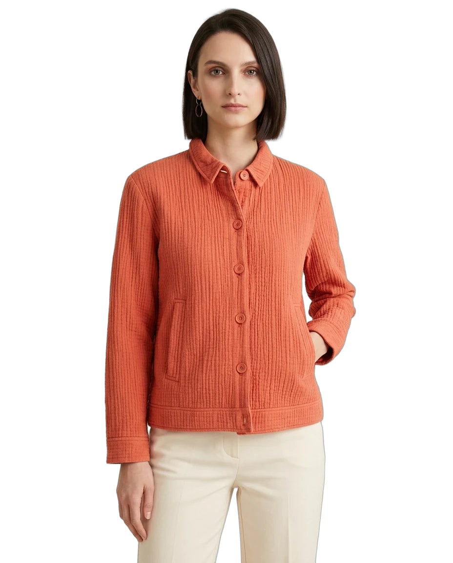 A woman modeling a textured, ribbed orange button-up cardigan with a collar and front pockets, paired with cream pants, against a plain white background.