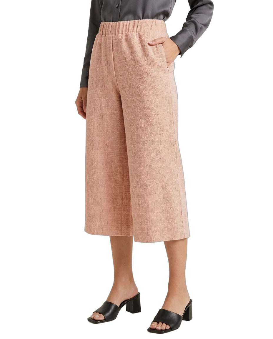 A model wearing a pair of high-waisted, wide-leg cropped pants in a textured dusty pink fabric, paired with a dark gray long-sleeve top and black block-heel slide sandals, set against a plain white background.
