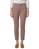 A model wearing slim-fit, ankle-length trousers in a dusty rose pink color, paired with a white long-sleeve blouse and brown leather loafers, shown against a plain white background.