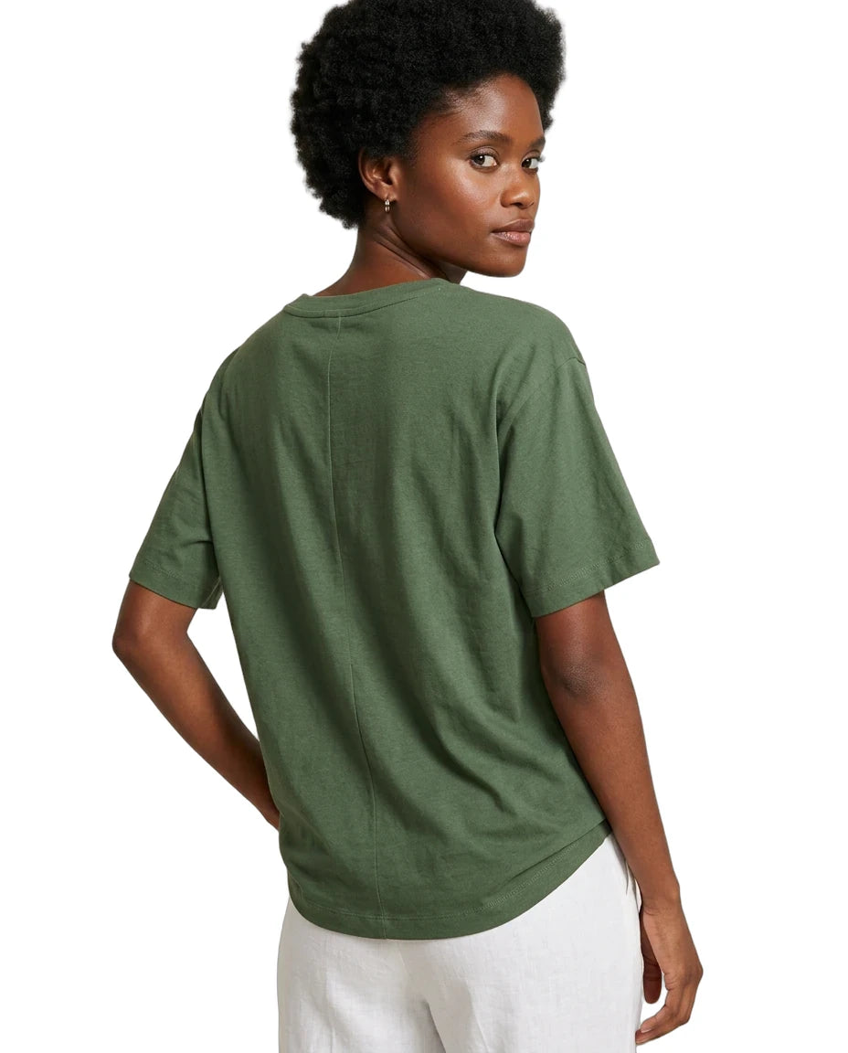 A woman shown from the back wearing an oversized short-sleeve crewneck t-shirt in olive green, paired with white pants, against a plain white background.