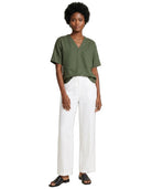 A woman modeling a short-sleeve olive green V-neck top and white wide-leg pants with black sandals, photographed against a plain white background.