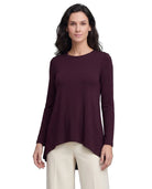 A woman modeling a long-sleeve high-low top in deep burgundy, paired with light beige pants, against a plain white background.