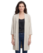 Woman wearing a beige cardigan over a black top and blue jeans on a white background
