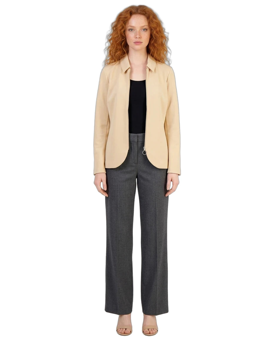 A model with curly red hair stands against a white background wearing a light beige blazer over a black top, paired with dark gray wide-leg trousers and beige flat sandals.
