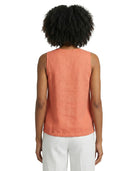 Person wearing a coral sleeveless top and white pants on a white background