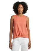 Woman wearing a coral sleeveless top and white pants on a white background