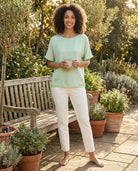 Woman standing outdoors in a garden setting with potted plants and a wooden bench.