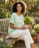 Woman sitting on a wooden bench in a garden holding a mug.