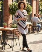 Woman in a patterned dress standing outdoors near a brick building with people in the background.