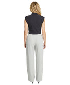 Woman wearing a black sleeveless top and light gray pants on a white background