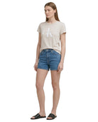 Woman wearing a beige Calvin Klein t-shirt and blue denim shorts on a white background