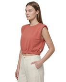 Woman wearing a sleeveless pink top and beige pants on a white background