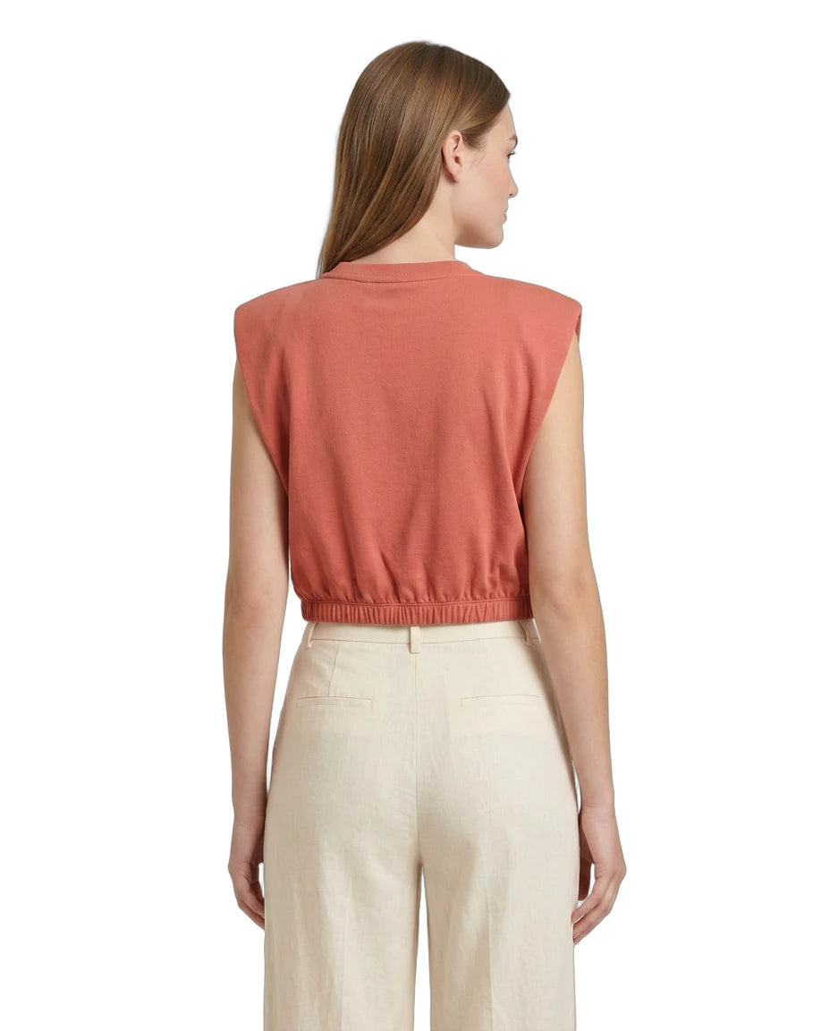 Woman wearing a sleeveless rust-colored top and beige pants on a white background