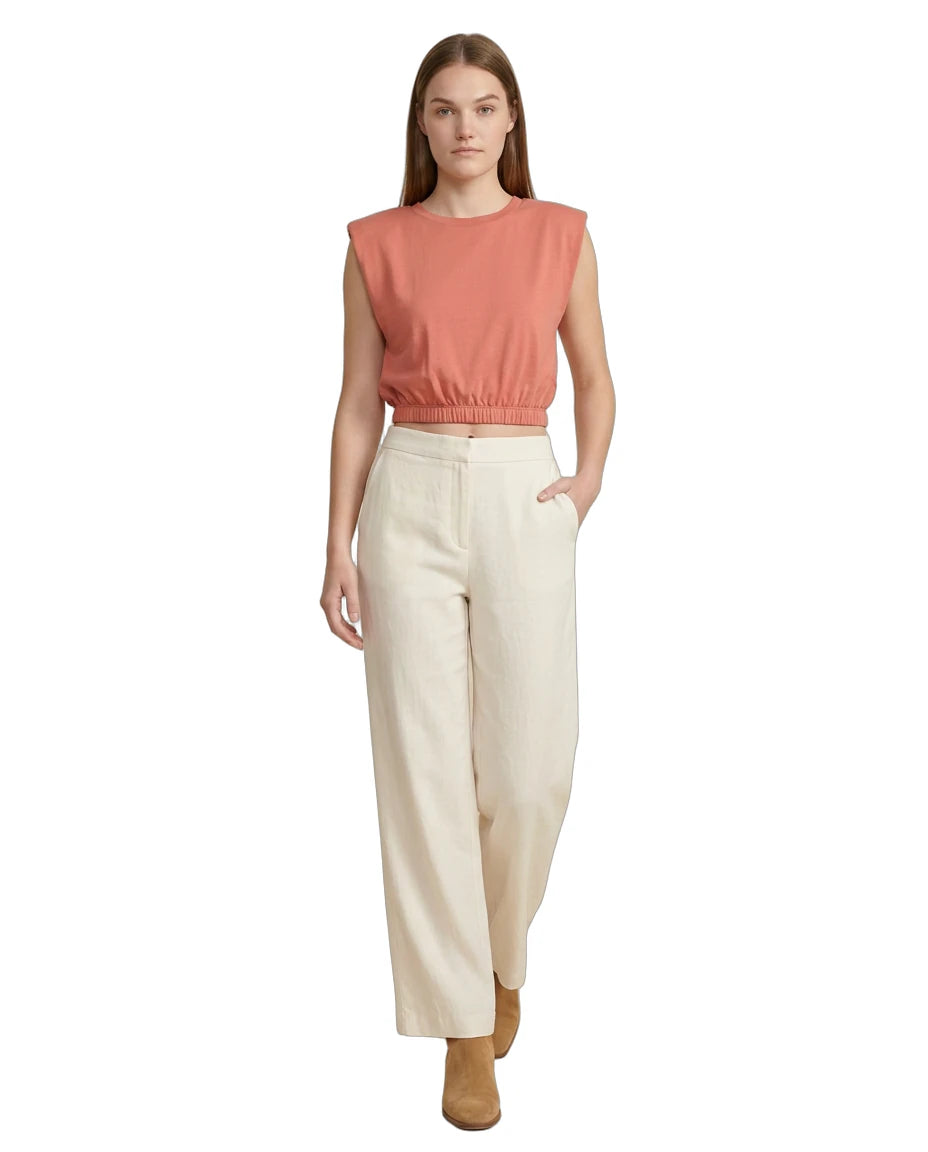 Woman wearing a coral sleeveless top and beige pants on a white background
