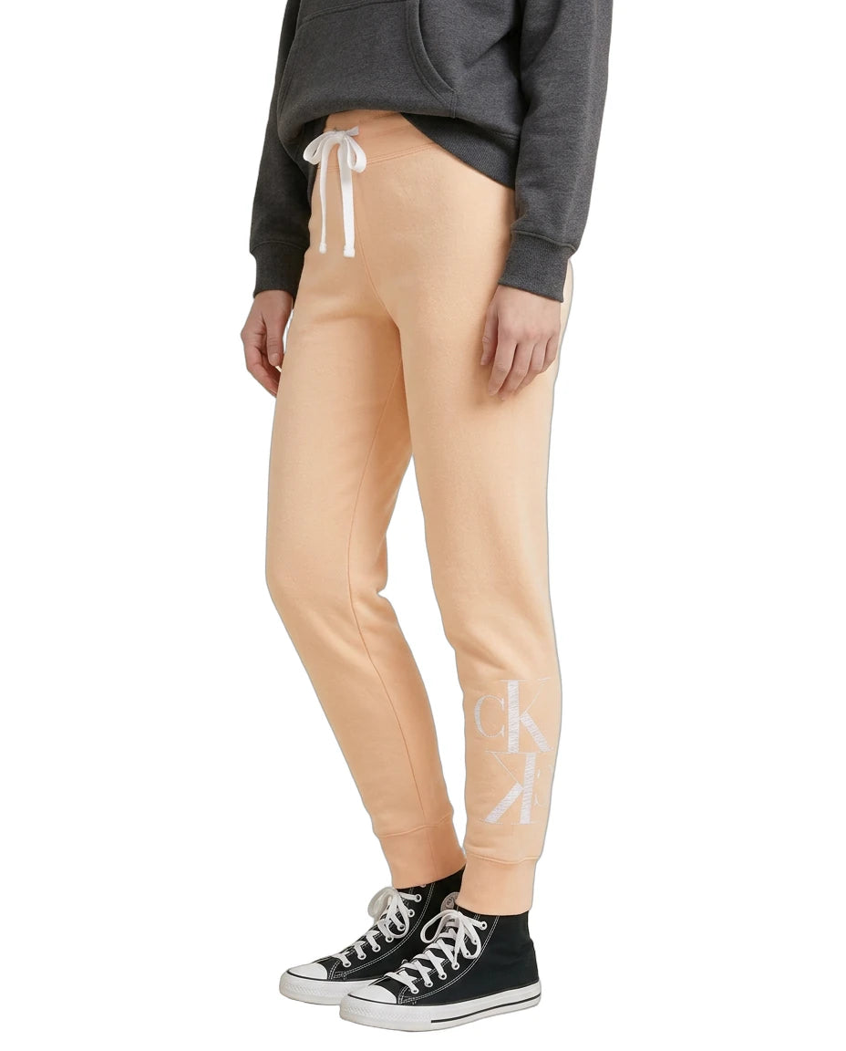 Person wearing beige jogger pants with a logo, black sneakers, and a gray sweatshirt on a white background.