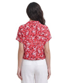 Woman wearing a red floral Calvin Klein blouse with white pants on a white background