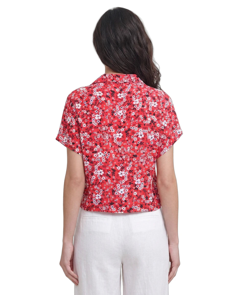 Woman wearing a red floral Calvin Klein blouse with white pants on a white background