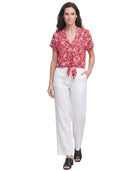 Woman wearing a red floral Calvin Klein blouse and white pants on a white background
