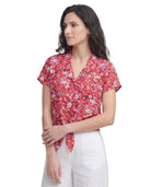 Woman wearing a red floral Calvin Klein blouse against a white background
